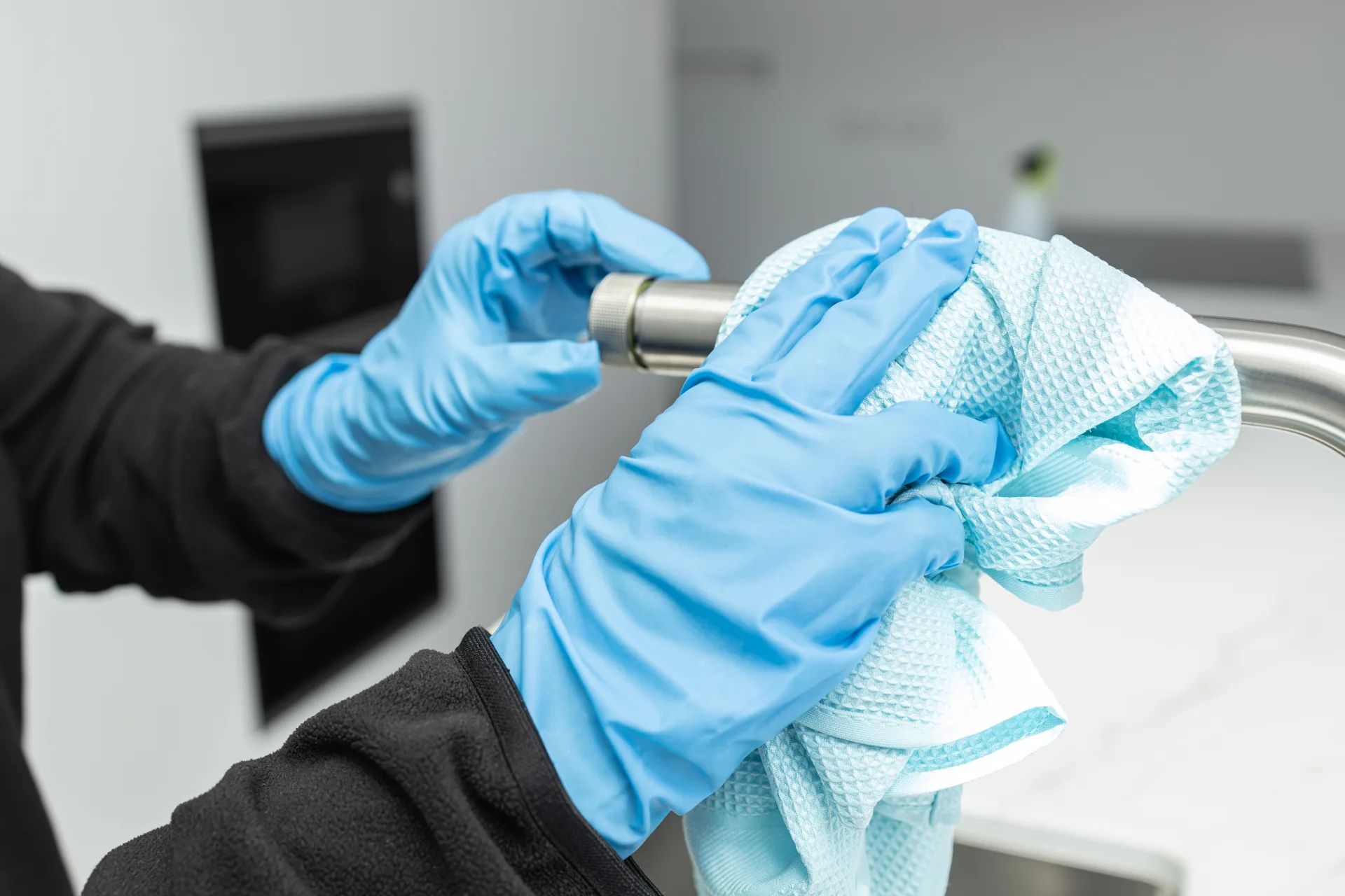 Gloved hands polishing a chrome kitchen tap with a cloth